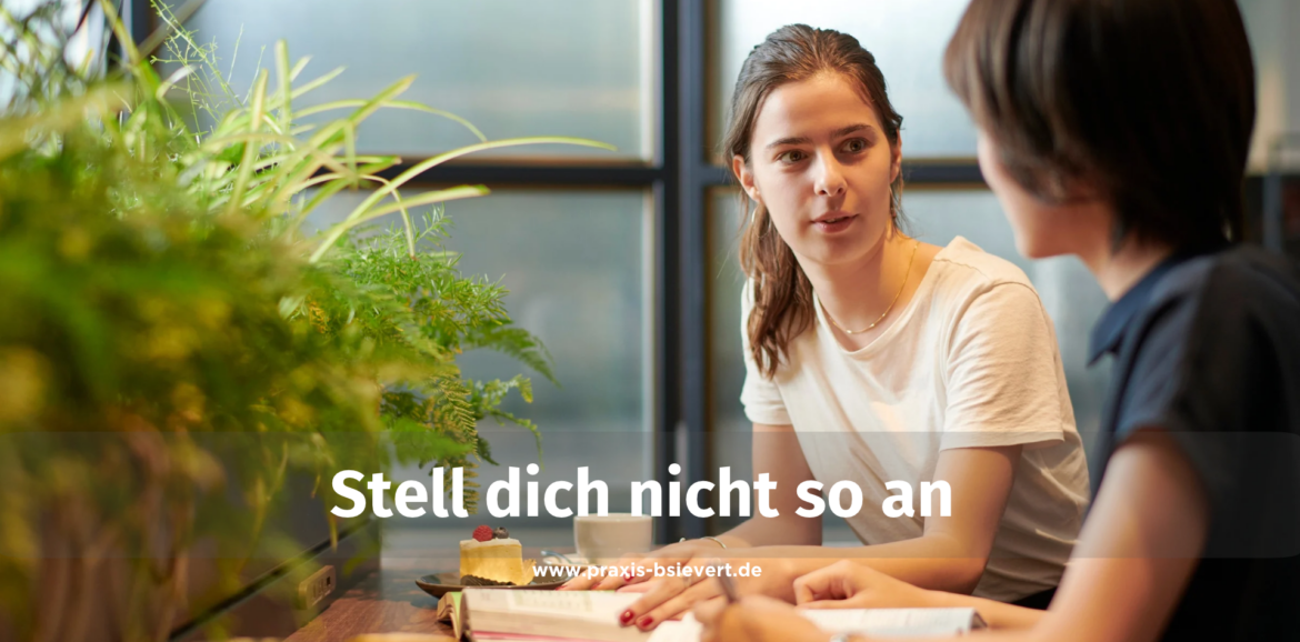 Zwei Frauen sitzen sich an einem Tisch im Café gegenüber und sprechen miteinander, eine Pflanze im Vordergrund, im Bild der Text „Stell dich nicht so an"